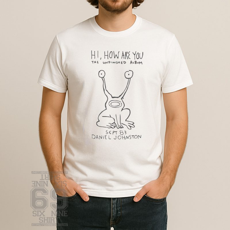 T-shirt with a hand-drawn cartoon frog character and the text “Hi, How Are You” and “The Unfinished Album” in handwritten font, based on Daniel Johnston's artwork.